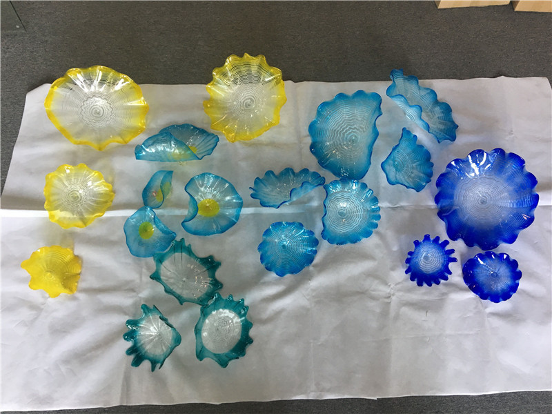 Contemporary Murano glass decorative wall plates featuring floral designs in blue and yellow hues with scalloped edges, handcrafted through traditional blowing techniques